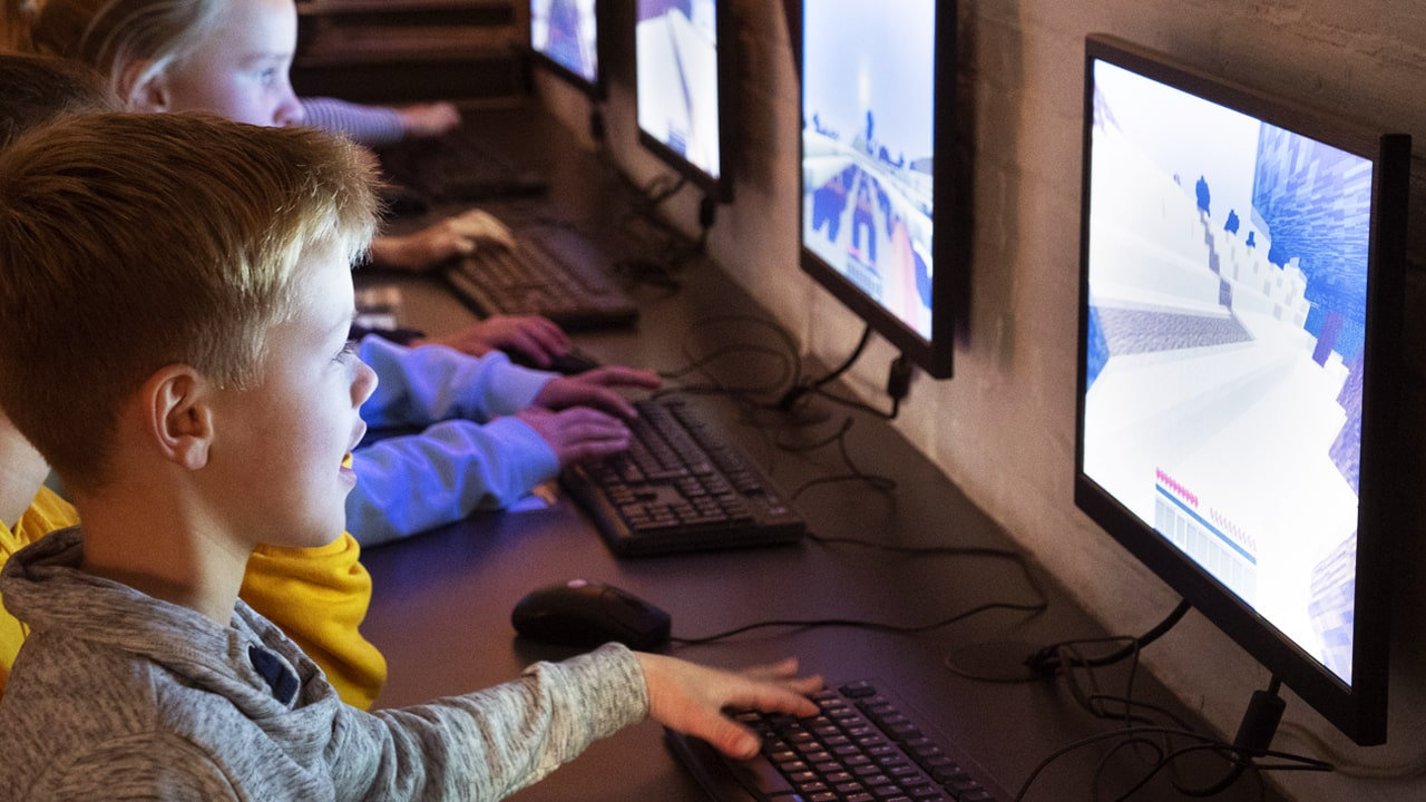 Kinderen zitten achter een computer en doen mee aan de workshop Minecraft.